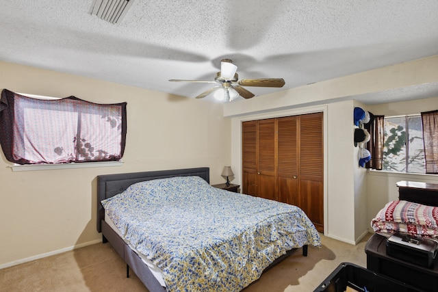 bedroom with ceiling fan, a closet, light carpet, and a textured ceiling