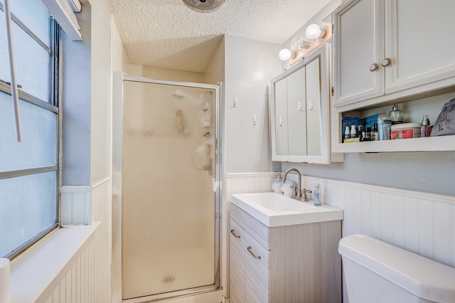 bathroom with vanity, toilet, a shower with door, and a textured ceiling