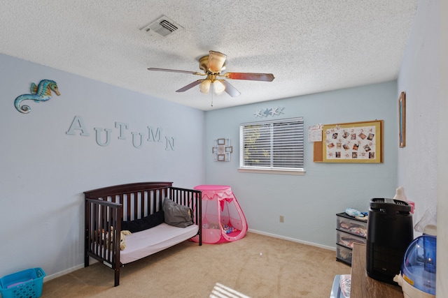 carpeted bedroom with a textured ceiling, ceiling fan, and a crib