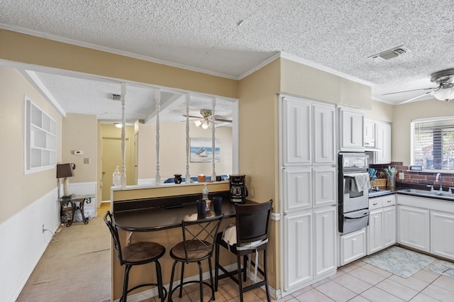 kitchen featuring a kitchen bar, sink, white cabinets, and a textured ceiling