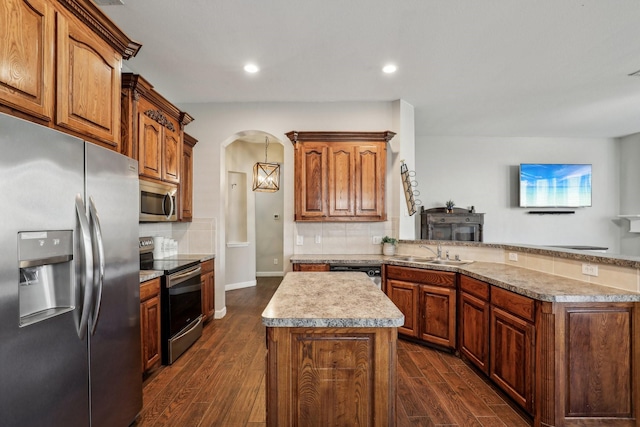 kitchen featuring arched walkways, dark wood finished floors, a peninsula, stainless steel appliances, and a sink