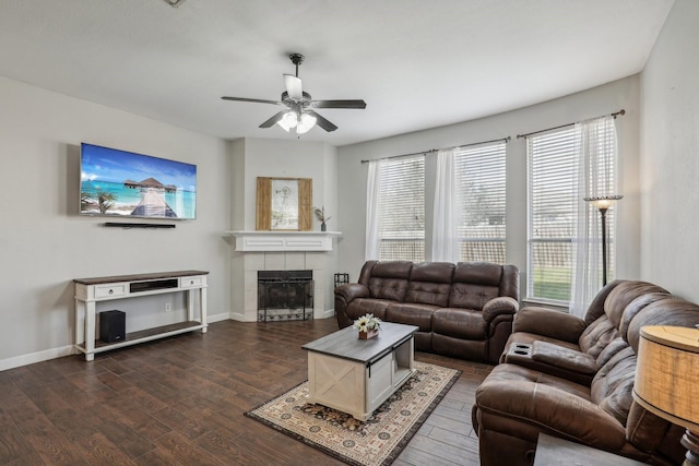 living area with a tile fireplace, dark wood-style flooring, ceiling fan, and baseboards