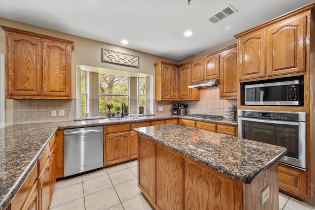 kitchen with appliances with stainless steel finishes, sink, dark stone countertops, a center island, and light tile patterned floors