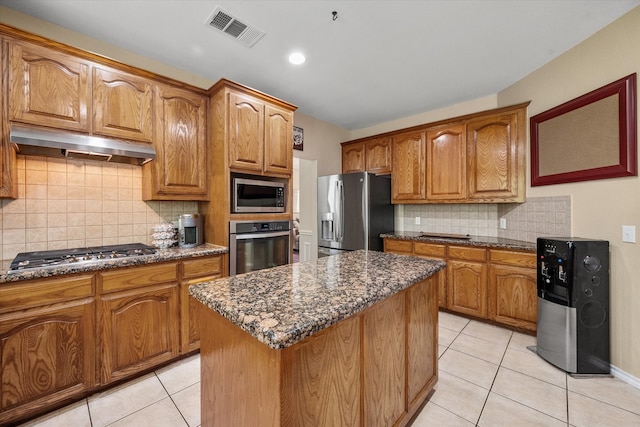 kitchen featuring decorative backsplash, dark stone countertops, light tile patterned floors, appliances with stainless steel finishes, and a kitchen island