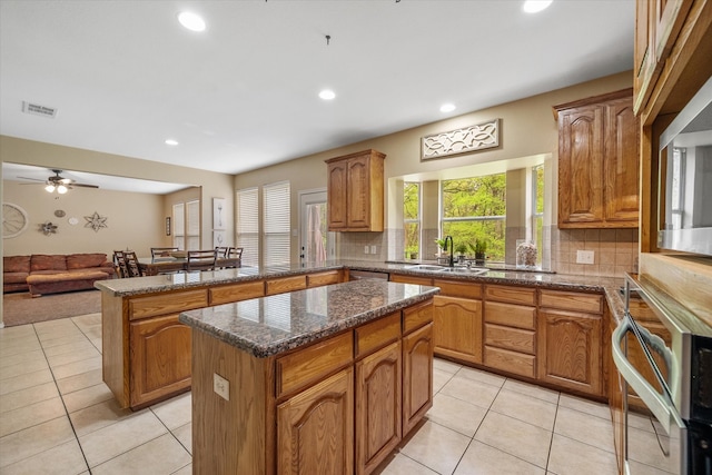 kitchen featuring kitchen peninsula, backsplash, sink, dark stone countertops, and a kitchen island