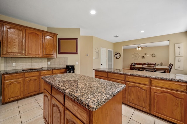 kitchen with decorative backsplash, a center island, ceiling fan, and dark stone countertops