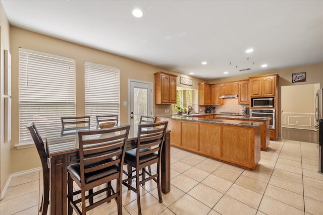 kitchen featuring sink, stainless steel appliances, tasteful backsplash, dark stone counters, and light tile patterned flooring