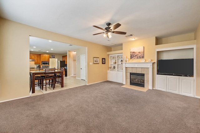 living room featuring ceiling fan, light colored carpet, and a tile fireplace