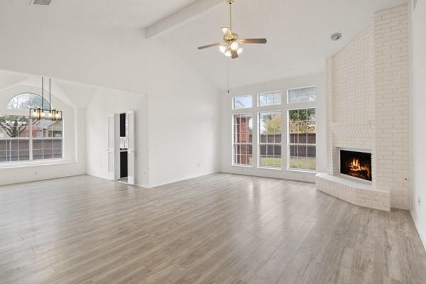 unfurnished living room featuring ceiling fan with notable chandelier, beam ceiling, high vaulted ceiling, a fireplace, and light hardwood / wood-style floors