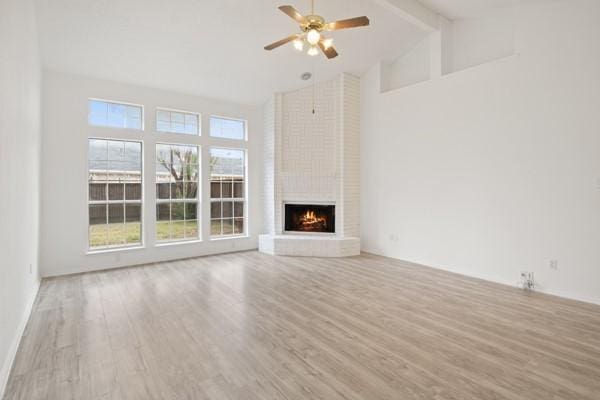 unfurnished living room with ceiling fan, a brick fireplace, beamed ceiling, high vaulted ceiling, and light hardwood / wood-style floors