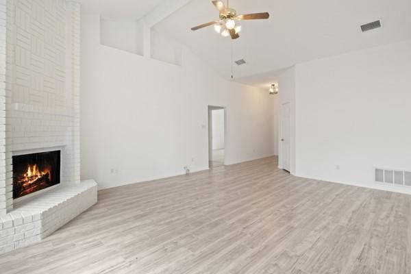 unfurnished living room featuring high vaulted ceiling, ceiling fan, light wood-type flooring, a fireplace, and beam ceiling