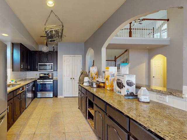 kitchen featuring dark brown cabinetry, light stone countertops, light tile patterned floors, and appliances with stainless steel finishes