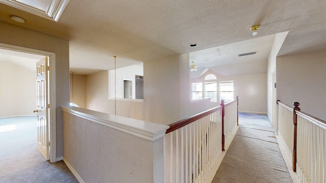 corridor with lofted ceiling, light colored carpet, and a textured ceiling