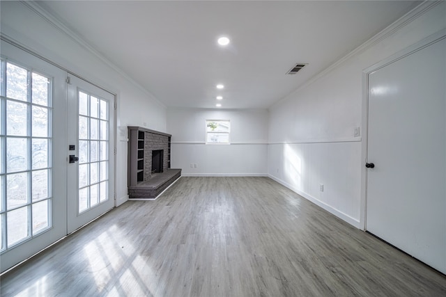 unfurnished living room with hardwood / wood-style floors, ornamental molding, french doors, and a brick fireplace