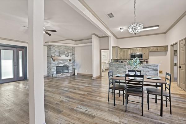 dining room featuring ceiling fan with notable chandelier, a fireplace, ornamental molding, and wood-type flooring