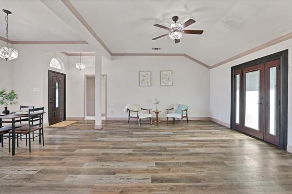 entrance foyer featuring wood-type flooring, vaulted ceiling, ornamental molding, and ceiling fan with notable chandelier