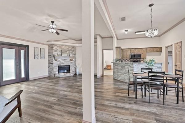 dining space featuring dark hardwood / wood-style flooring, ceiling fan with notable chandelier, a fireplace, and ornamental molding