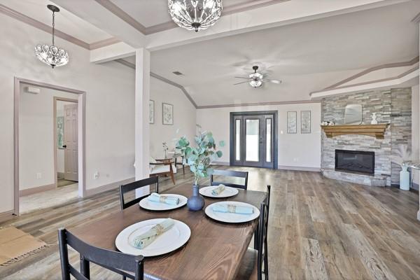 dining area featuring a stone fireplace, lofted ceiling with beams, ornamental molding, hardwood / wood-style flooring, and ceiling fan with notable chandelier