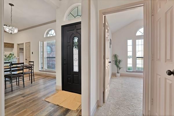 foyer entrance featuring crown molding, lofted ceiling, wood-type flooring, and a notable chandelier