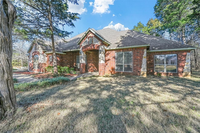 view of front of house featuring brick siding, a front lawn, and a shingled roof