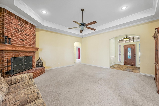 unfurnished living room featuring carpet, arched walkways, a tray ceiling, and ornamental molding