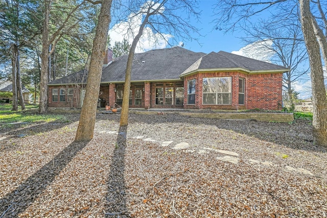 view of front facade with brick siding, a chimney, and a shingled roof