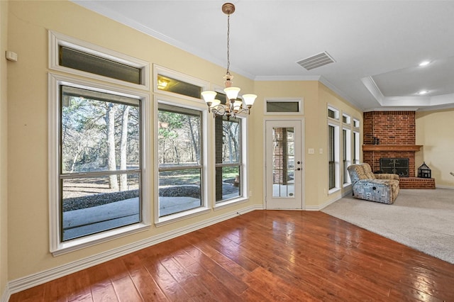 interior space with a raised ceiling, crown molding, a brick fireplace, a notable chandelier, and wood-type flooring