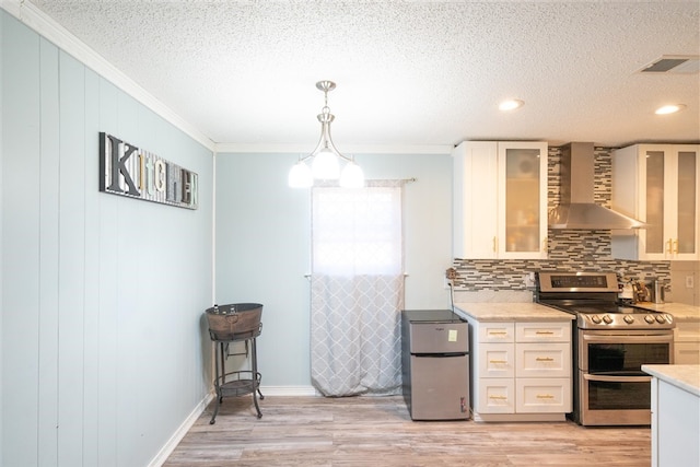 kitchen featuring appliances with stainless steel finishes, wall chimney exhaust hood, light hardwood / wood-style floors, white cabinetry, and hanging light fixtures