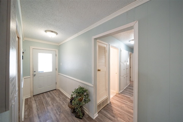 entryway with a textured ceiling, light wood-type flooring, and crown molding