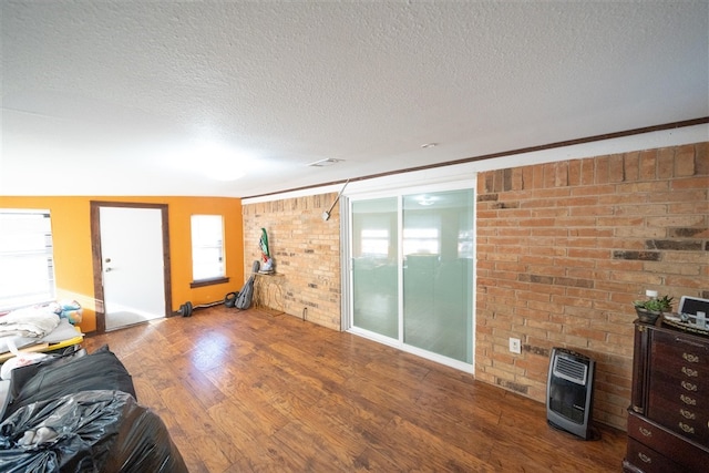 unfurnished living room featuring wood-type flooring, a textured ceiling, heating unit, and brick wall