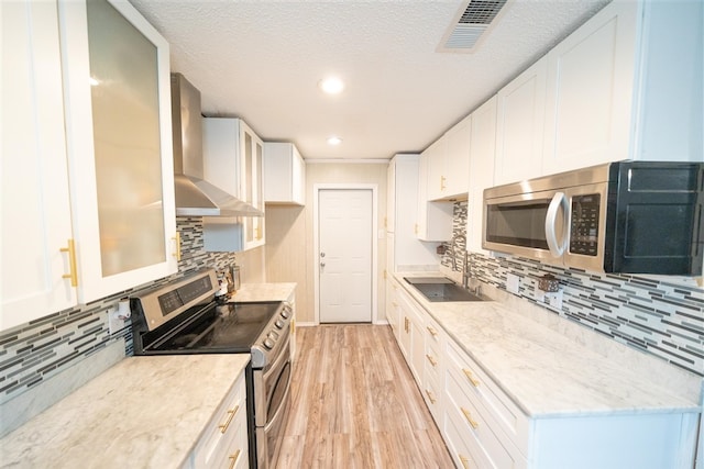 kitchen with white cabinets, decorative backsplash, stainless steel appliances, and wall chimney range hood