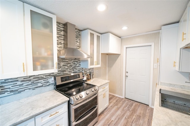 kitchen featuring wall chimney range hood, light wood-type flooring, white cabinets, and stainless steel electric range