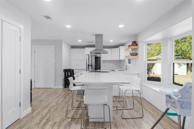 kitchen with white cabinetry, stainless steel appliances, light hardwood / wood-style floors, a breakfast bar area, and island range hood