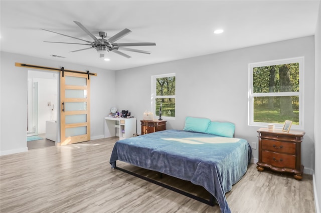 bedroom featuring multiple windows, a barn door, light hardwood / wood-style floors, and ceiling fan