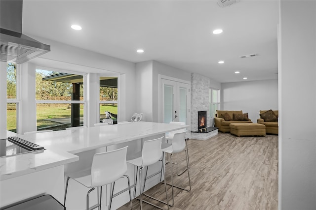 kitchen featuring island range hood, light wood-type flooring, a fireplace, and a breakfast bar area