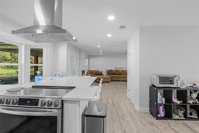 kitchen with light stone counters, light wood-type flooring, wall chimney range hood, and stainless steel range with electric cooktop