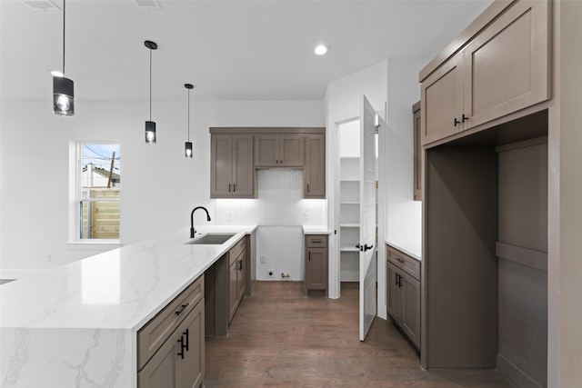 kitchen with backsplash, sink, light stone countertops, decorative light fixtures, and dark hardwood / wood-style flooring