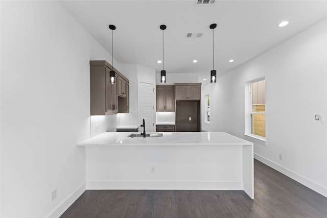 kitchen with kitchen peninsula, pendant lighting, dark wood-type flooring, and sink