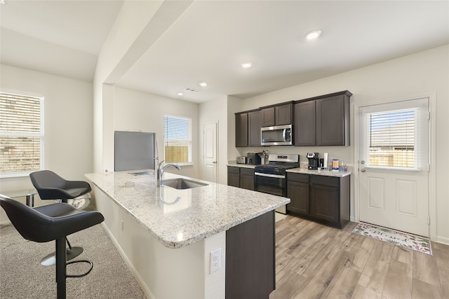 kitchen featuring sink, light hardwood / wood-style flooring, appliances with stainless steel finishes, dark brown cabinets, and light stone counters