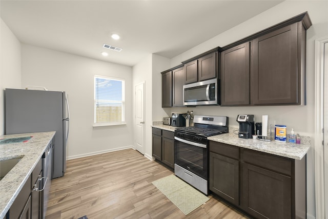 kitchen with light stone countertops, light wood-type flooring, stainless steel appliances, and dark brown cabinetry