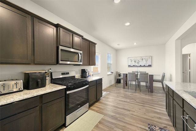 kitchen featuring light stone countertops, dark brown cabinetry, appliances with stainless steel finishes, and light hardwood / wood-style flooring