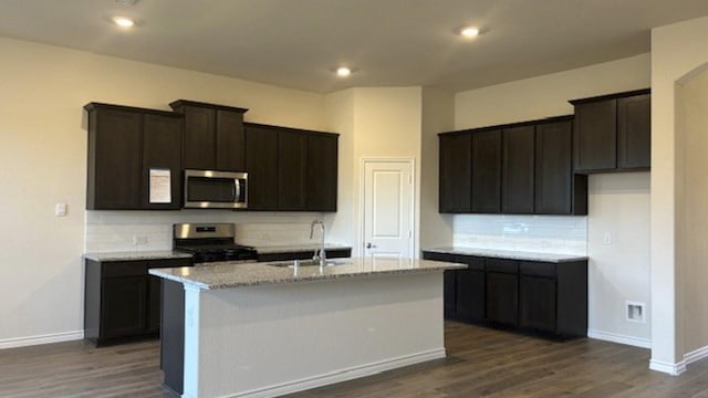 kitchen featuring appliances with stainless steel finishes, sink, dark hardwood / wood-style floors, a kitchen island with sink, and light stone counters