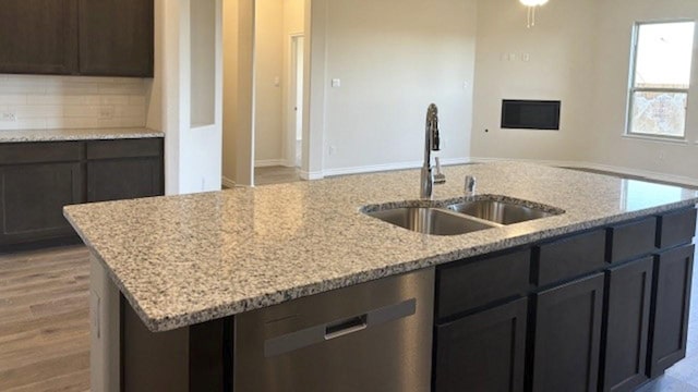 kitchen with tasteful backsplash, sink, a kitchen island with sink, light stone counters, and stainless steel dishwasher