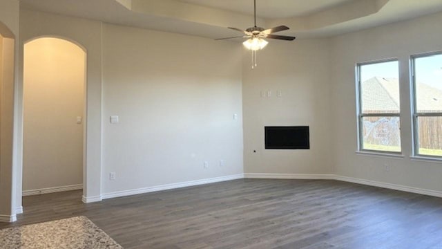 unfurnished living room featuring ceiling fan, a raised ceiling, and dark hardwood / wood-style flooring