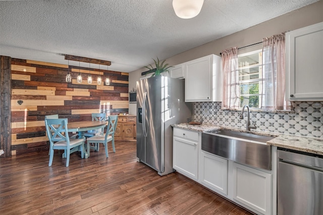 kitchen with pendant lighting, white cabinets, appliances with stainless steel finishes, sink, and wood walls