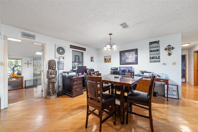 dining area with a textured ceiling, light hardwood / wood-style floors, and an inviting chandelier