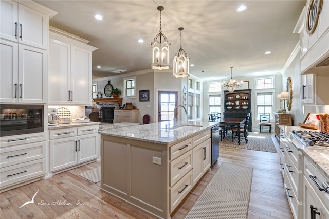 kitchen with ornamental molding, sink, pendant lighting, light hardwood / wood-style flooring, and an island with sink