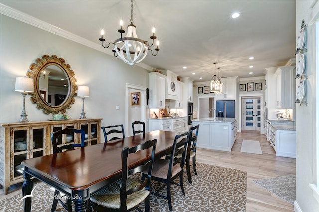 dining area featuring sink, a notable chandelier, light hardwood / wood-style flooring, and ornamental molding