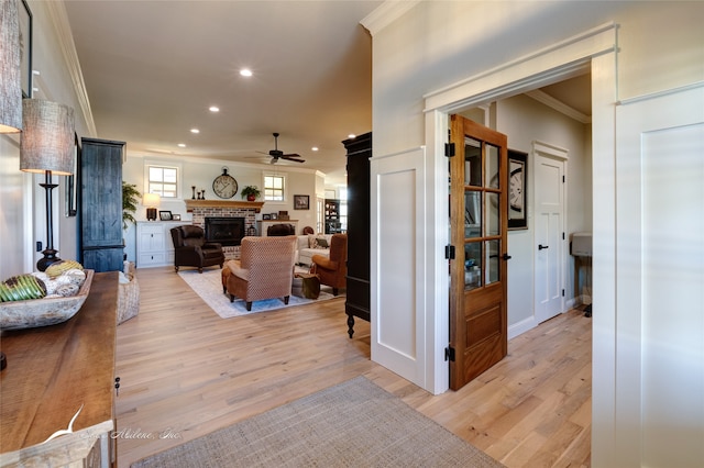 living room with a brick fireplace, ceiling fan, crown molding, and light wood-type flooring