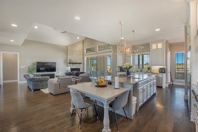 dining area featuring sink, a stone fireplace, dark hardwood / wood-style floors, a chandelier, and vaulted ceiling